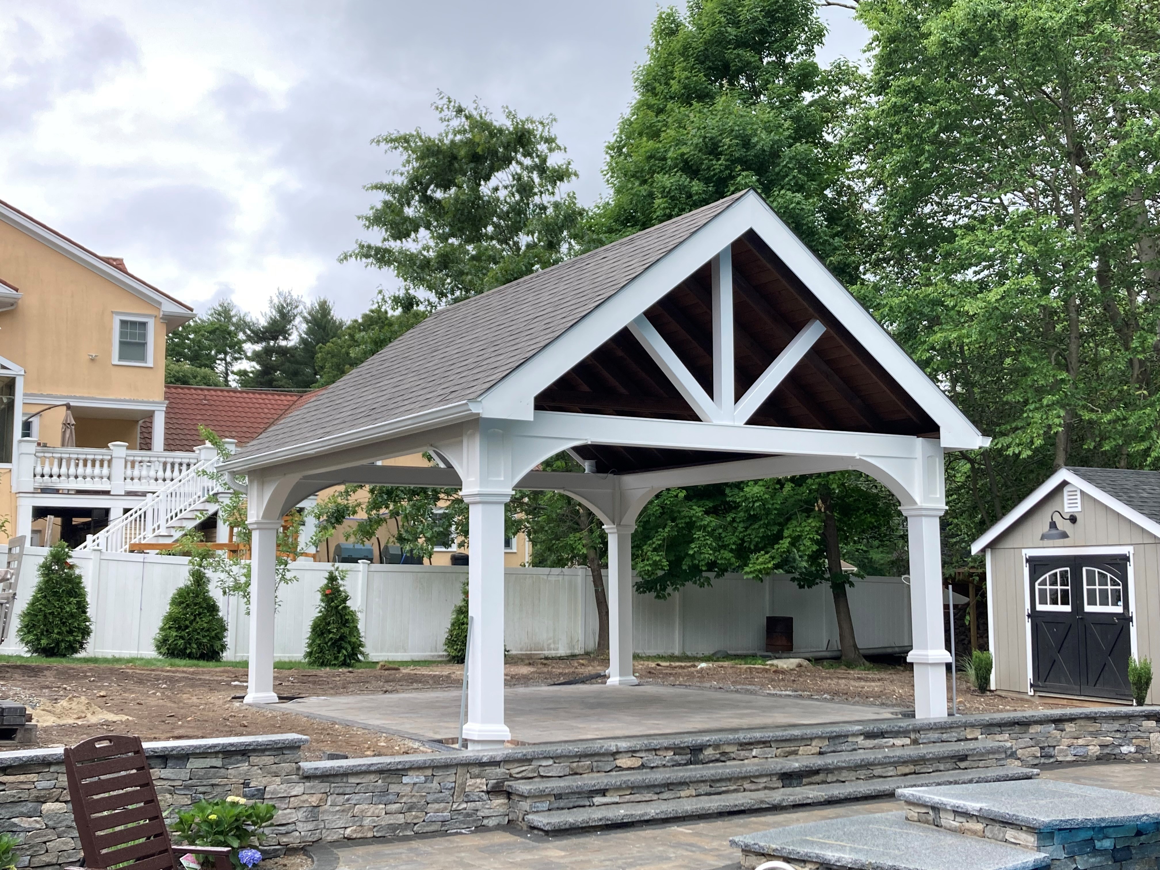 Wood-framed pavilion with metal roof, stone fireplace, and outdoor sofa