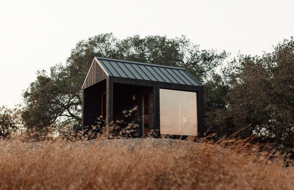 Weathered wood sauna with covered porch and glass front in a backyard setting