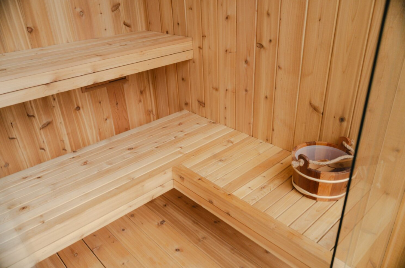 Wood-shingled sauna with metal roof glowing warmly at dusk in the woods