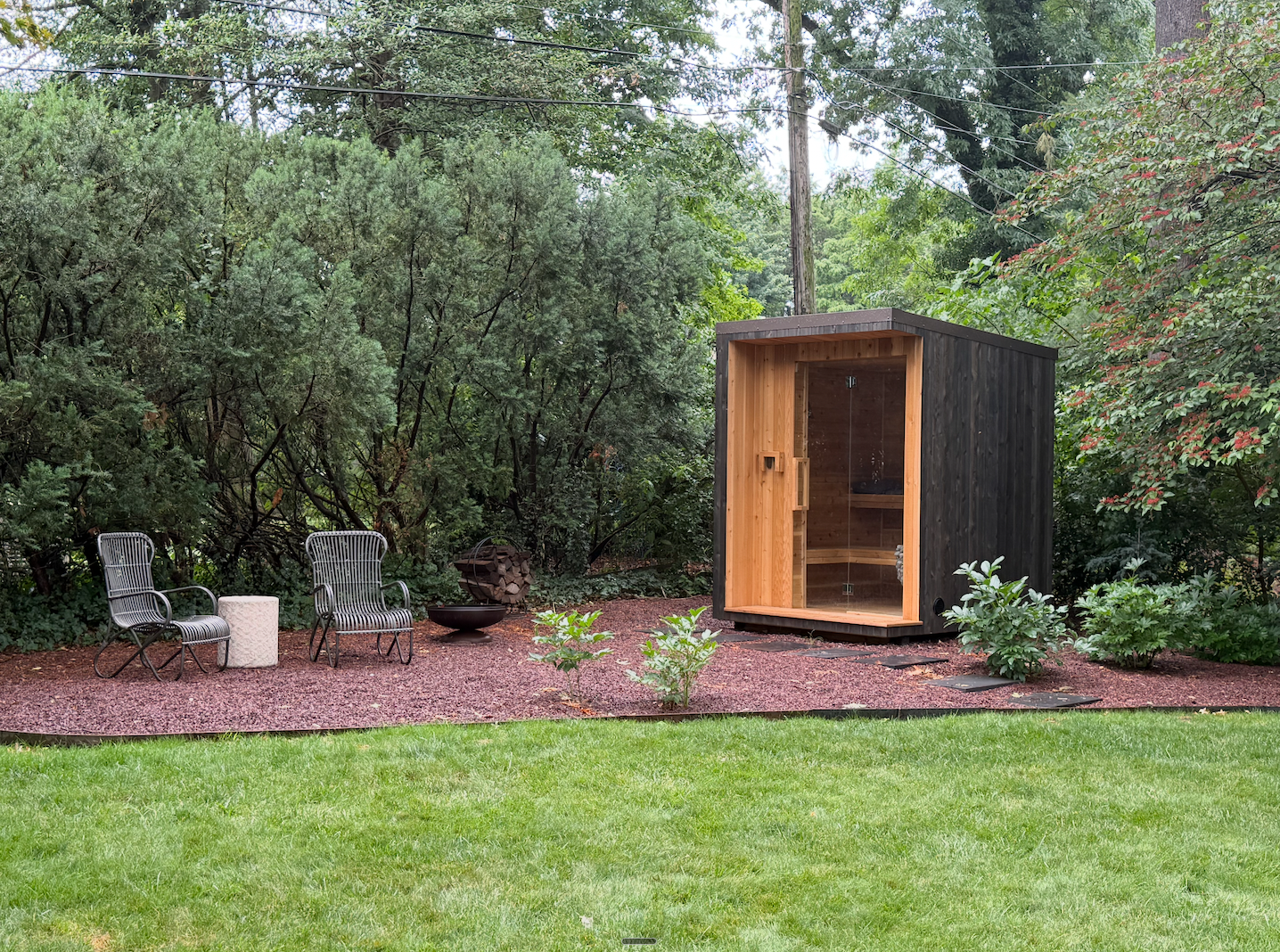 Cedar shingle sauna exterior with large glass window framed by greenery